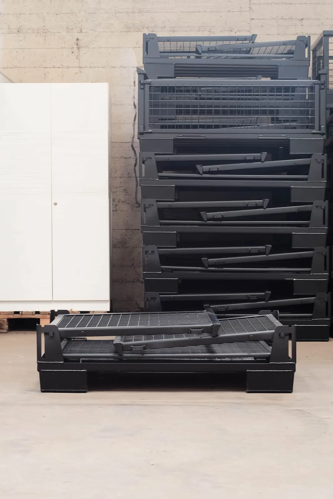 Gitterbox halb zusammengefaltet vor einem Stapel flacher Boxen im Lager